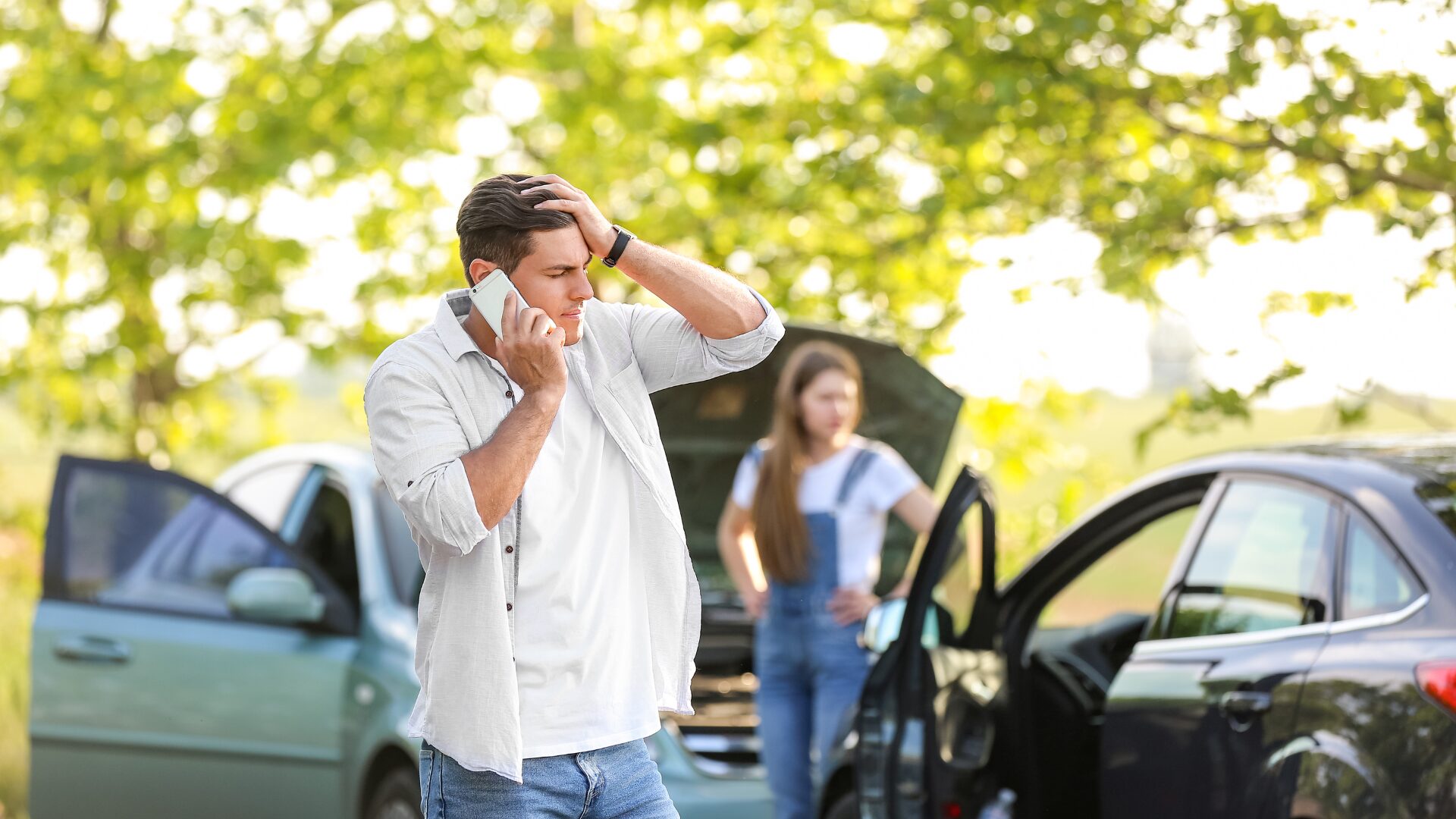 Two cars have had an accident. A man is frustrated with his hand on his head whilst he deals with his incident.