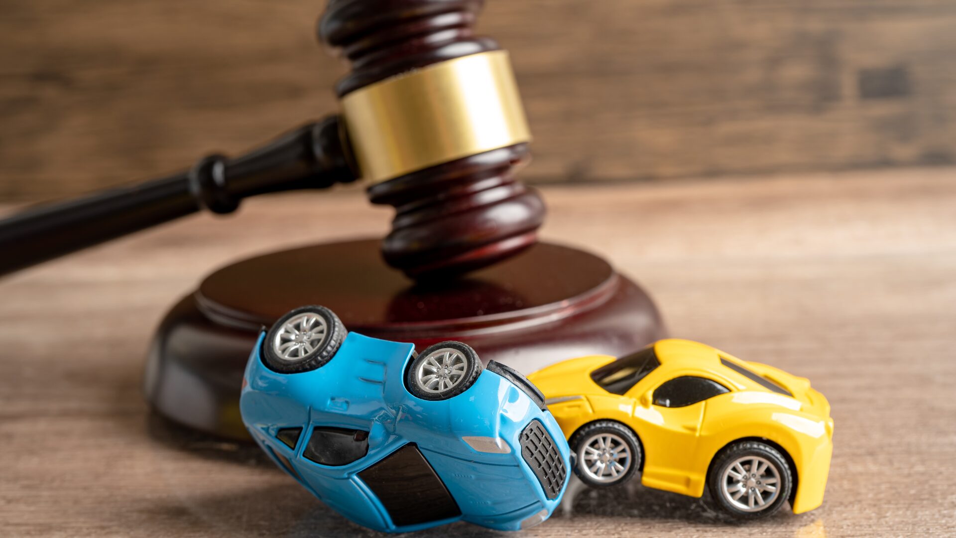 Two toy cars, one flipped over after an accident. Beside a court hammer. This visualises Motor Legal Cover.